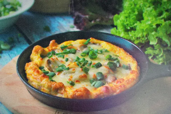 A cheesy egg omelet topped with green onions in a black cast iron skillet.