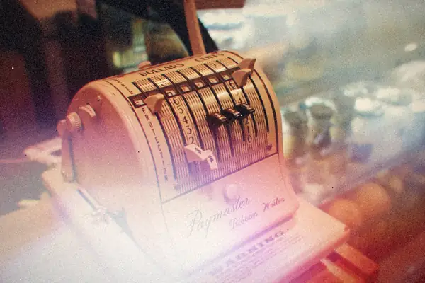 A vintage Paymaster adding machine sitting on a wooden cafe counter.