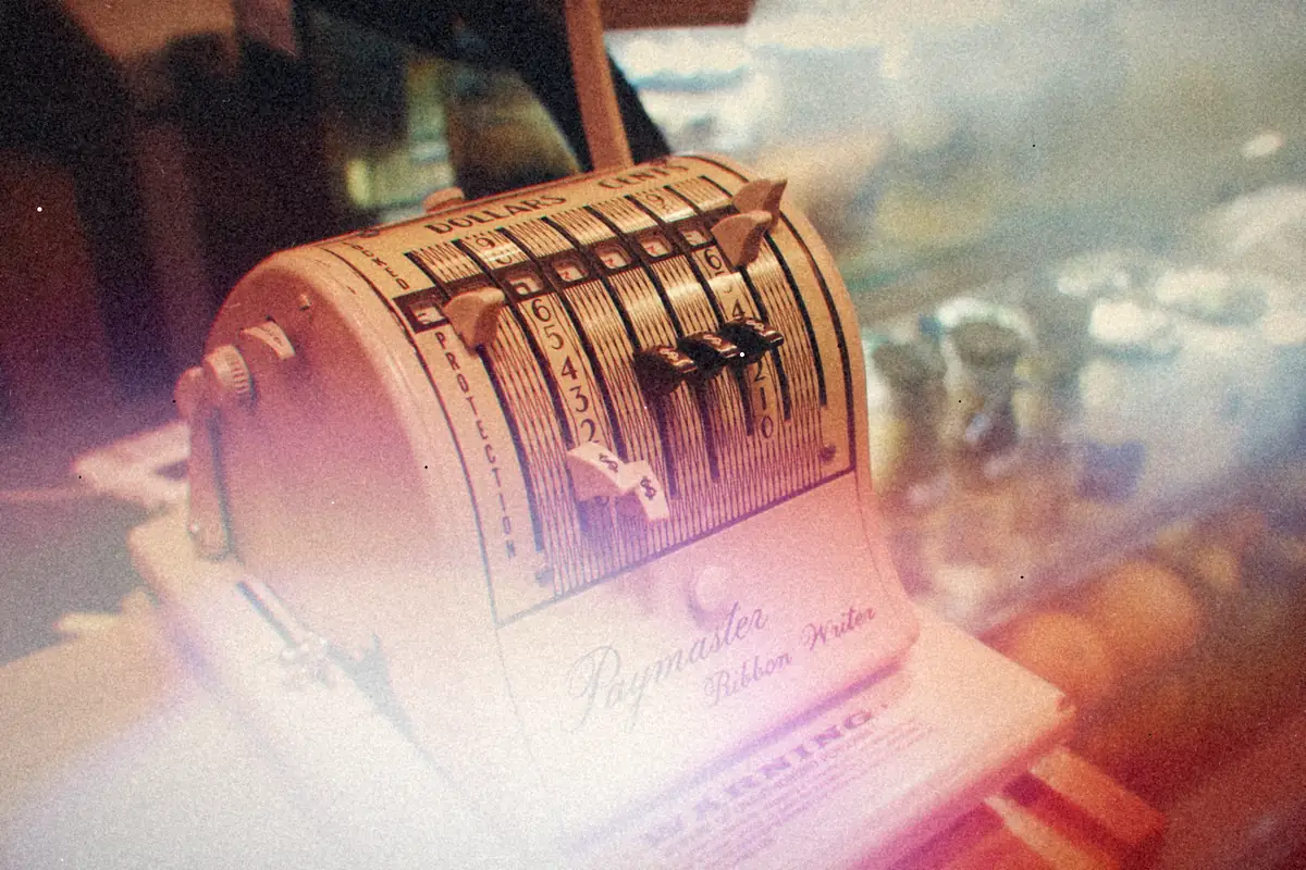 A vintage Paymaster adding machine sitting on a wooden cafe counter.