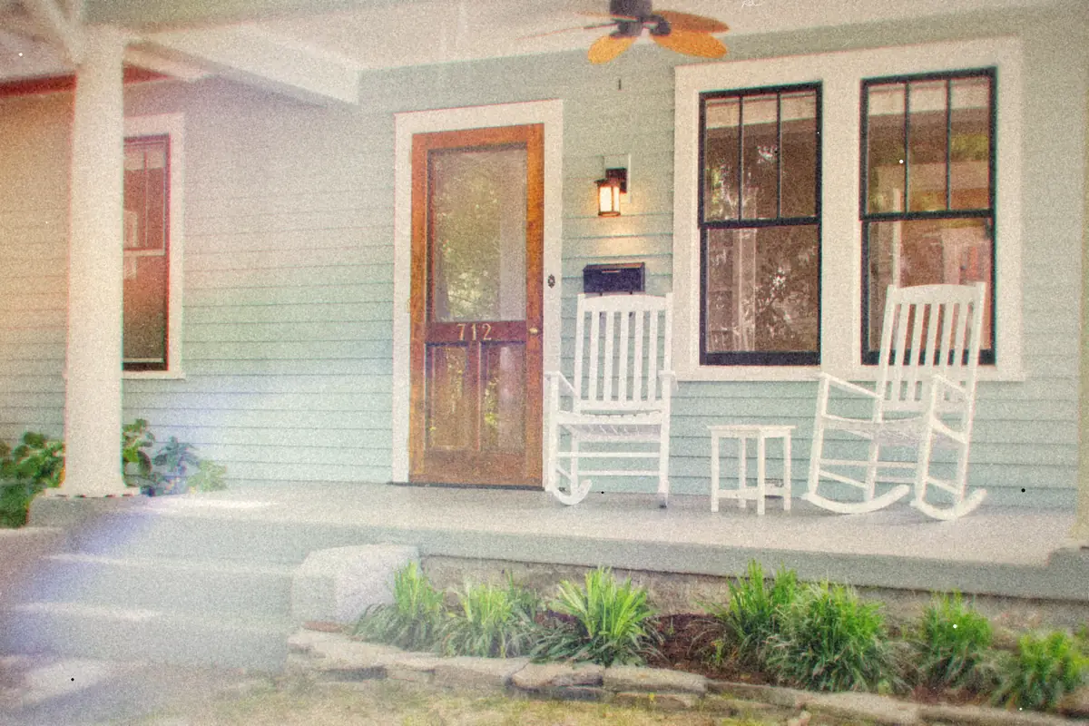 A front porch with white rocking chairs beside a wooden front door.