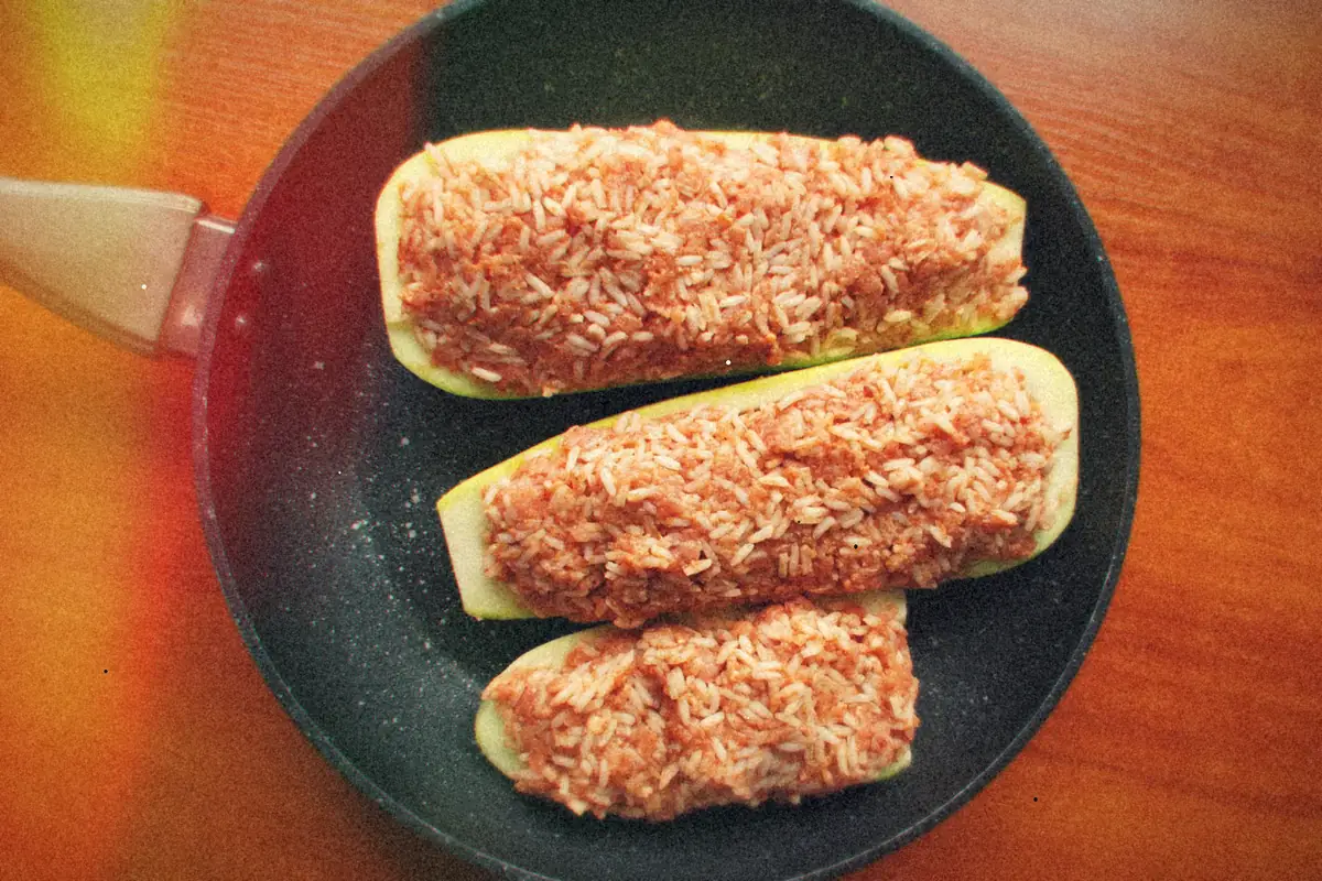 Three halved zucchini boats stuffed with a tomato and rice filling in a black skillet.