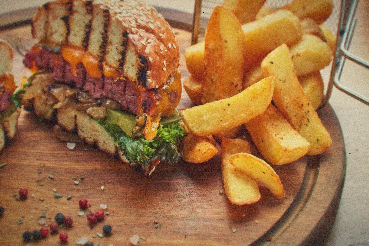 A sesame-bun cheeseburger with lettuce beside thick-cut fries on a wooden board.