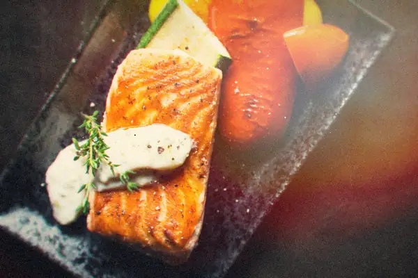 A seared salmon fillet with herb sauce and thyme beside roasted peppers and zucchini.