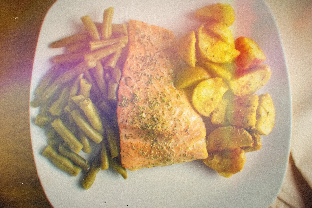 A herb-seasoned salmon fillet with green beans and roasted potatoes on a white plate.