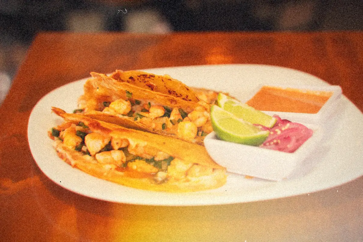 Crispy shrimp tacos on a white plate with lime wedges, pickled onions and salsa.