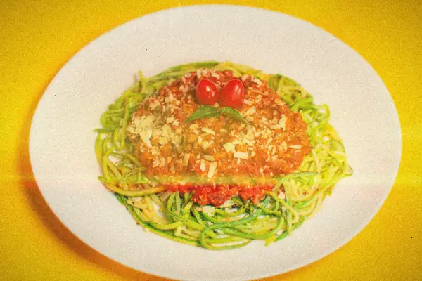 Zucchini noodles topped with meat sauce, grated cheese and cherry tomatoes on a white plate.