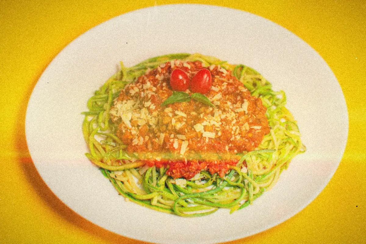Zucchini noodles topped with meat sauce, grated cheese and cherry tomatoes on a white plate.