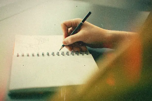 A hand sketching with a pen in a spiral notebook.