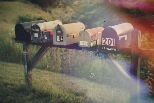 A row of rusty rural mailboxes on a wooden post in a grassy field.