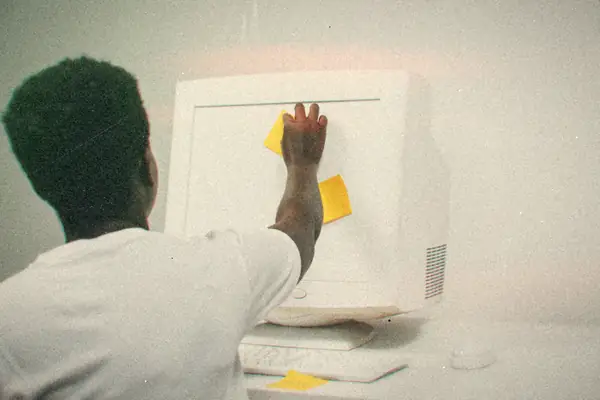 A person sticking yellow sticky notes on the side of an old beige CRT computer.