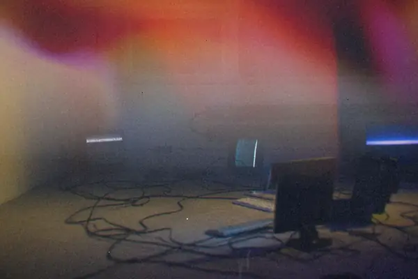 Old computers and CRT monitors with tangled cables in a dim room.