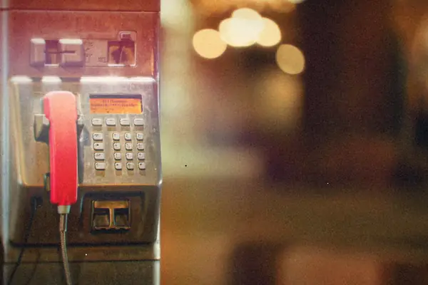 A coin payphone with a red handset on a city street.