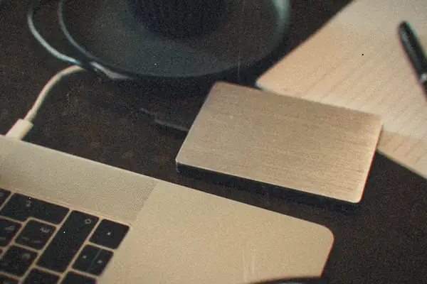 A silver external hard drive plugged into a laptop, next to a notepad and a pen.