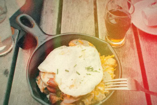 A fried egg over a meat and potato hash in a cast iron pan on a wooden table.
