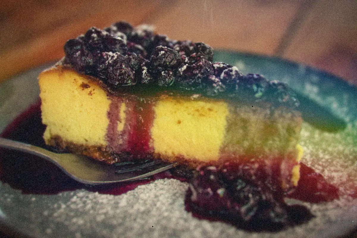 A slice of baked cheesecake piled with blueberry compote on a dark plate.