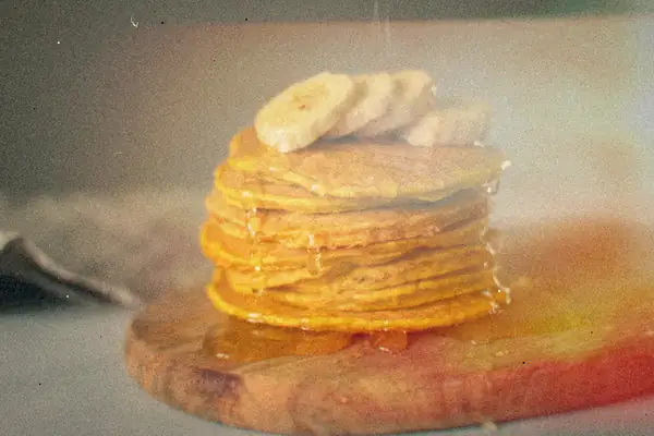 A stack of pancakes topped with banana slices and syrup on a wooden board.