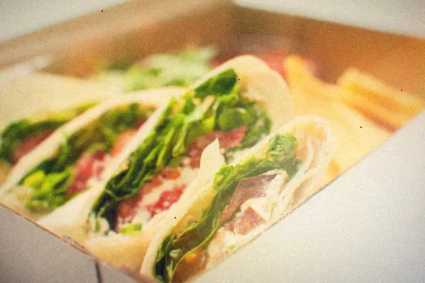 Halved tortilla wraps filled with lettuce, cured meat and a creamy spread, packed in a box with chips.