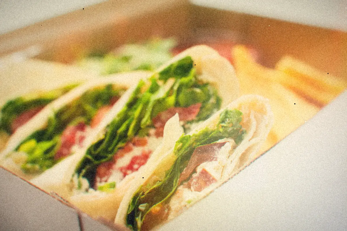 Halved tortilla wraps filled with lettuce, cured meat and a creamy spread, packed in a box with chips.