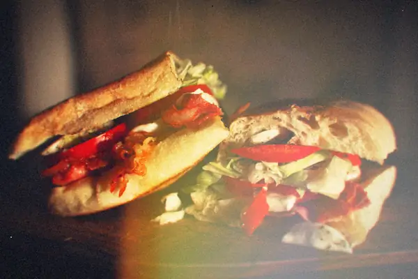 A bacon, lettuce and tomato sandwich cut in half on a dark board.