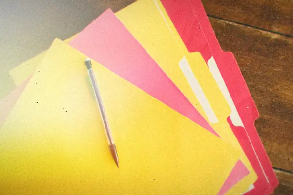 Bright yellow and pink paper file folders fanned out on a wooden table with a pen on top.