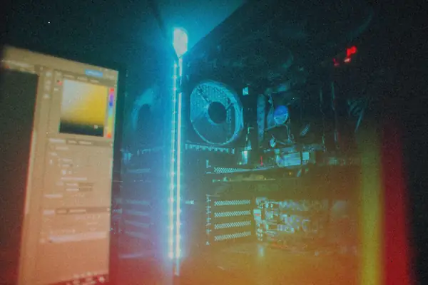 The inside of a desktop gaming PC lit up in blue, with case fans, a CPU cooler and graphics cards behind the side panel next to a monitor.