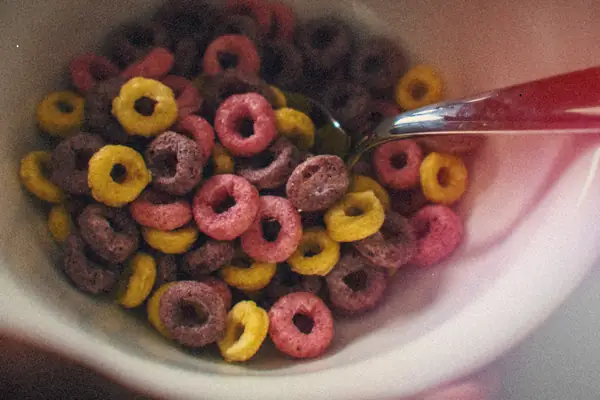 A white bowl of colorful fruity cereal rings with a spoon.