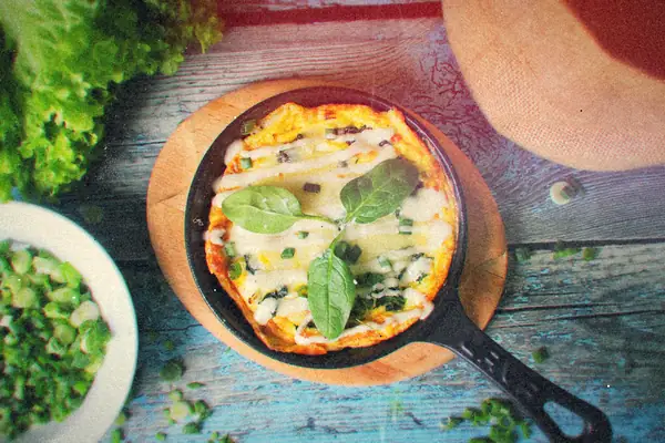 A cheesy omelet topped with chopped green onions in a small cast-iron skillet on a blue wooden table.