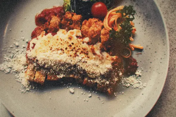 Breaded chicken parmigiana under browned melted cheese and tomato sauce with spaghetti on a gray plate.