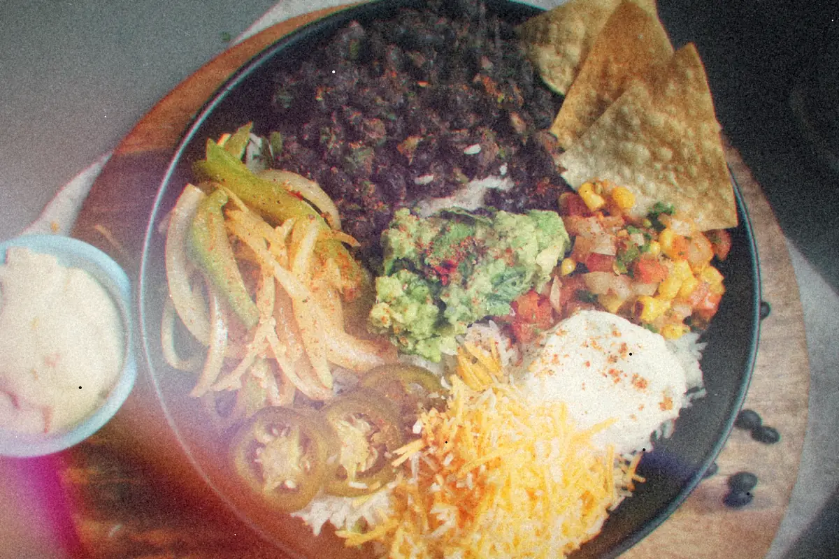 A burrito bowl with black beans, fajita peppers, guacamole, corn salsa, cheese and tortilla chips over rice.