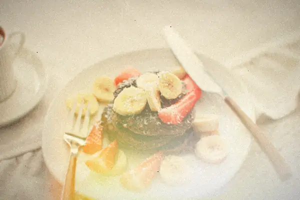 A short stack of chocolate pancakes topped with banana slices, strawberries and coconut flakes.