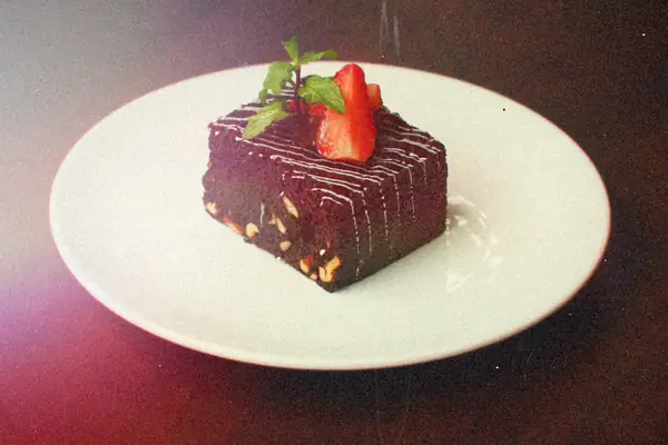 A chocolate brownie square topped with sliced strawberry and mint on a white plate.