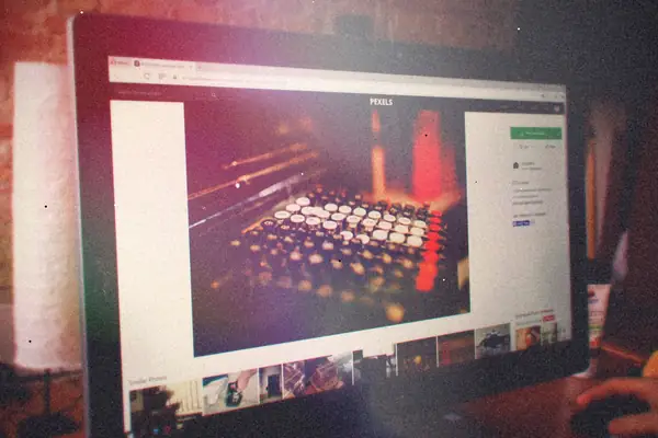 A desktop monitor with a web browser open, on a desk against a brick wall.