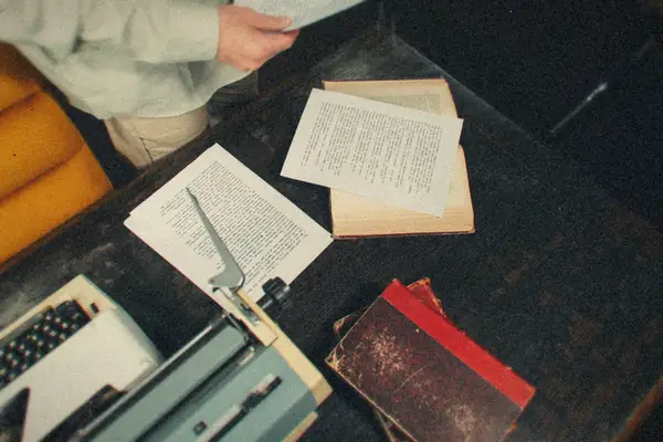 An overhead view of a wooden writing desk with a typewriter, typed manuscript pages and old books.
