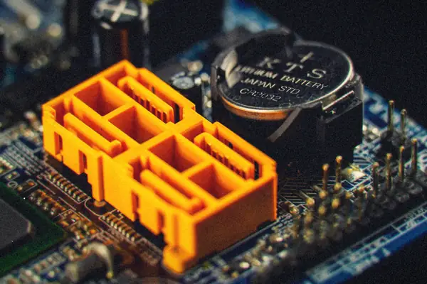 Close-up of a motherboard CMOS coin battery beside orange SATA connectors.