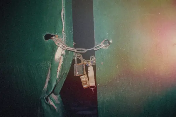 A rusty chain and padlock holding green metal doors shut.