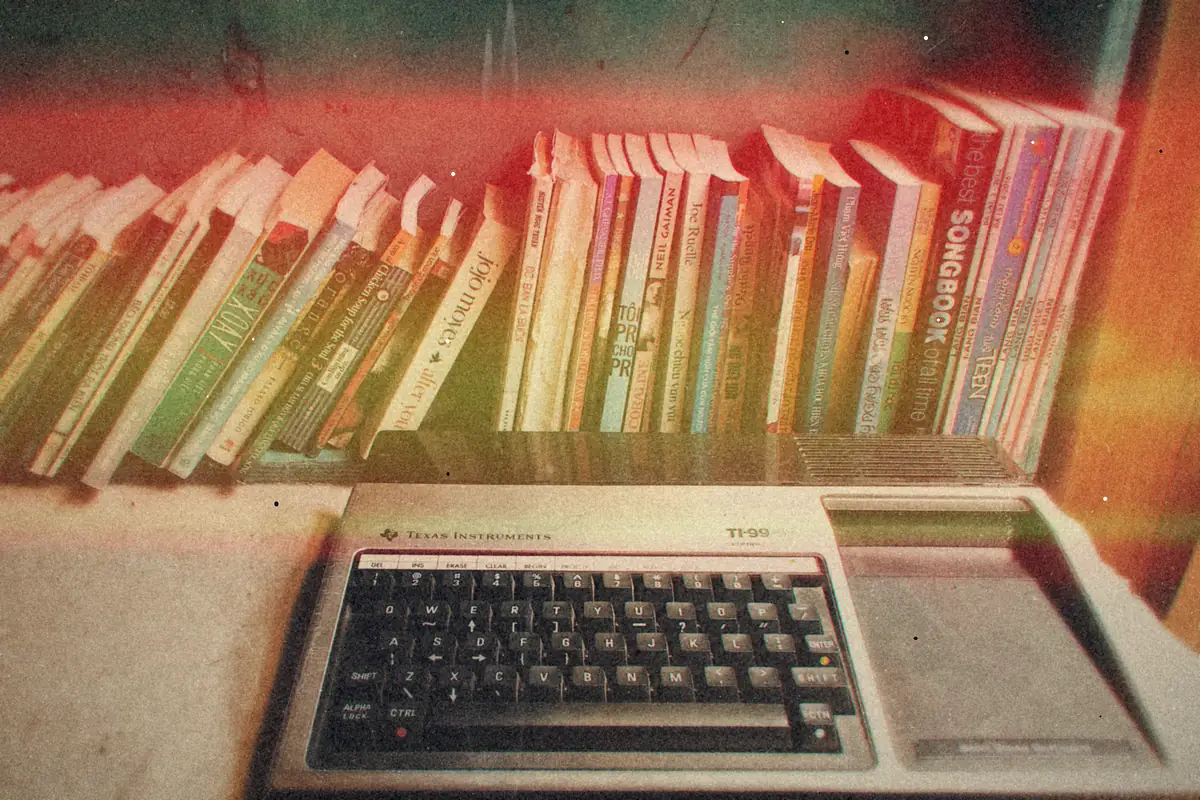 A beige vintage home computer keyboard sitting in front of a crowded bookshelf.