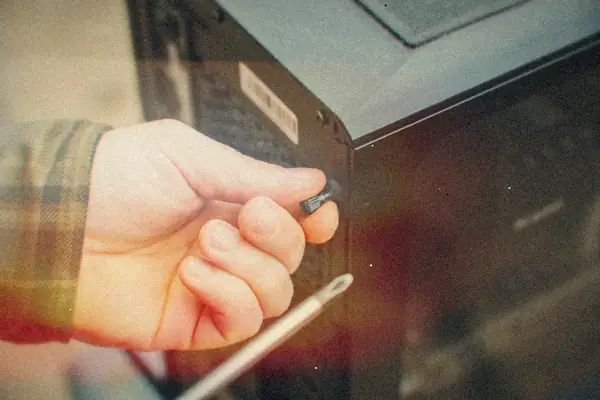A hand with a screwdriver unscrewing the side panel of a desktop PC case.