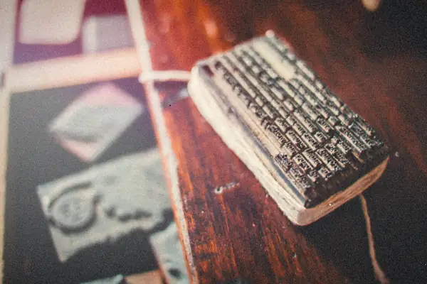 A block of metal letterpress type resting on a worn wooden printing table.