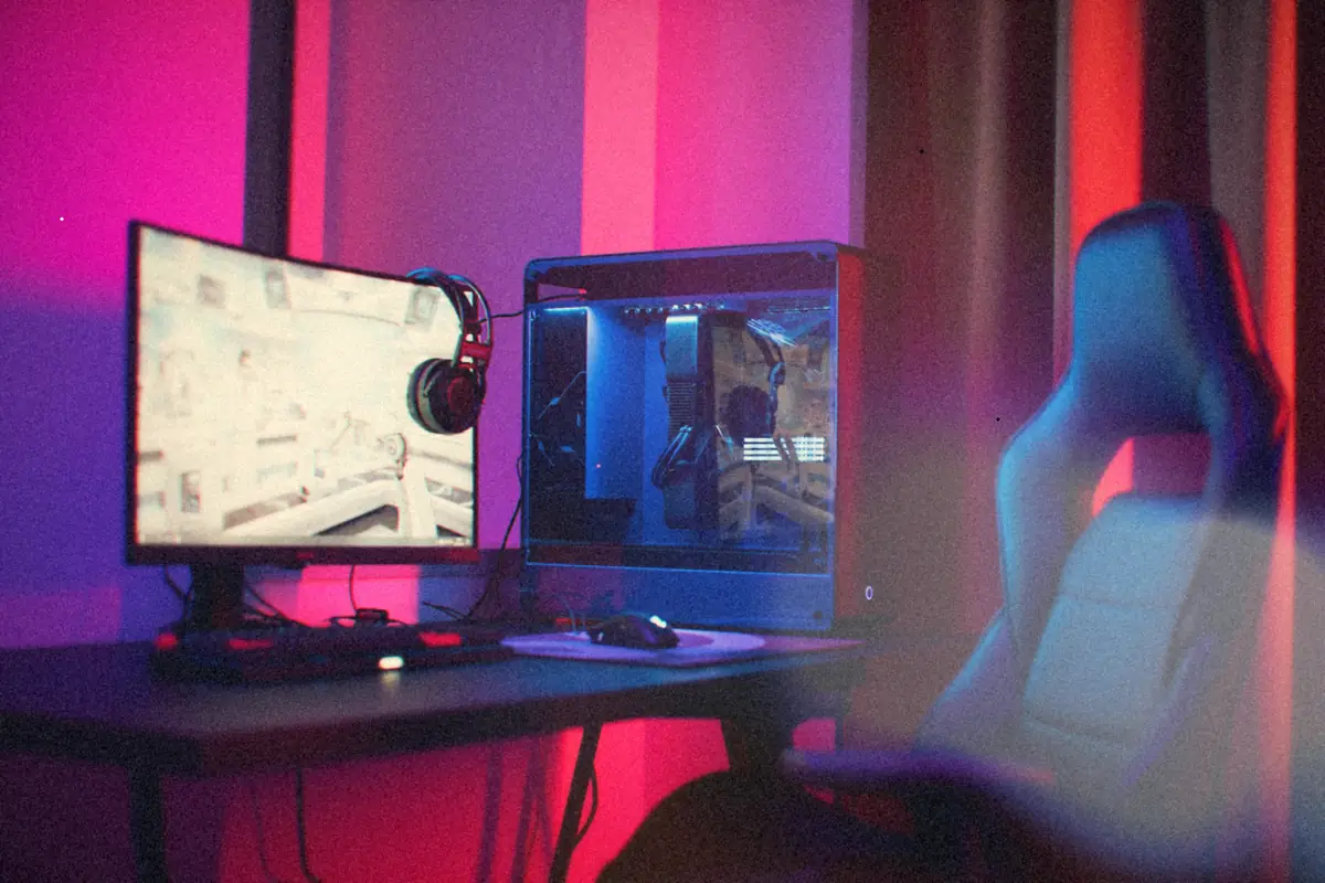 A gaming PC setup with a monitor, headphones, glass-sided tower and gaming chair under pink and purple light.