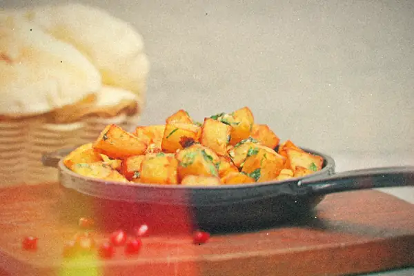 Cubed fried potatoes with herbs in a small cast iron skillet on a wooden board.