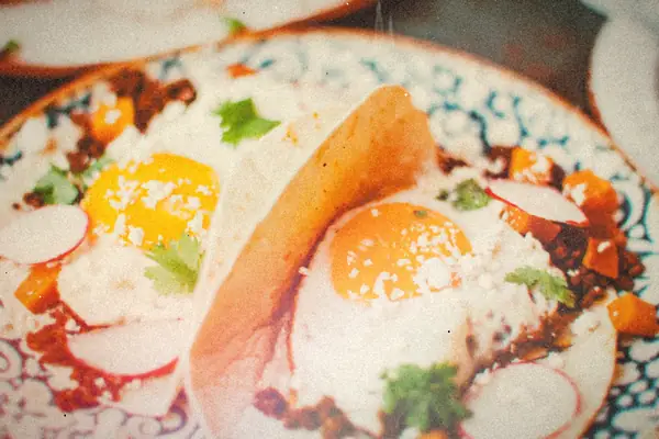 Flour tortilla breakfast tacos topped with fried eggs, crumbled sausage, radish slices and cilantro.