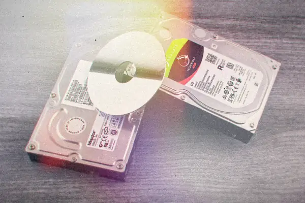 Two computer hard drives and a shiny disc lying on a wooden surface.