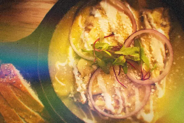 Enchiladas baked in green sauce with cream, red onion rings and microgreens in a cast iron skillet.