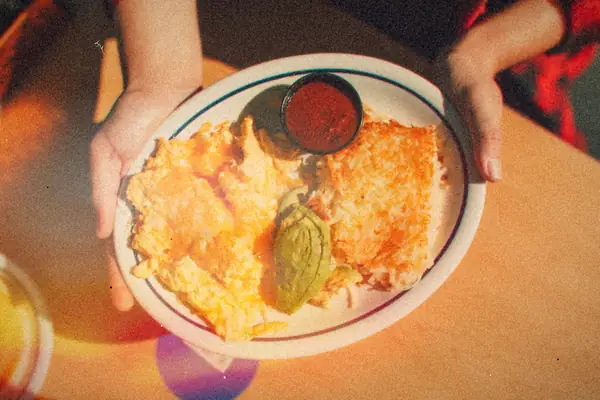 A plate of golden shredded hash browns with cheesy scrambled eggs, avocado and a cup of salsa.