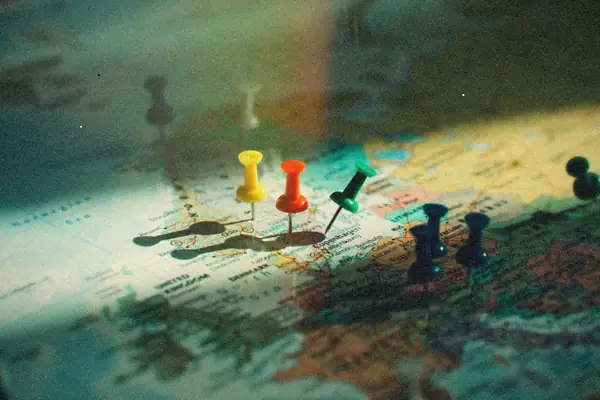Colorful push pins stuck into a map in raking sunlight.