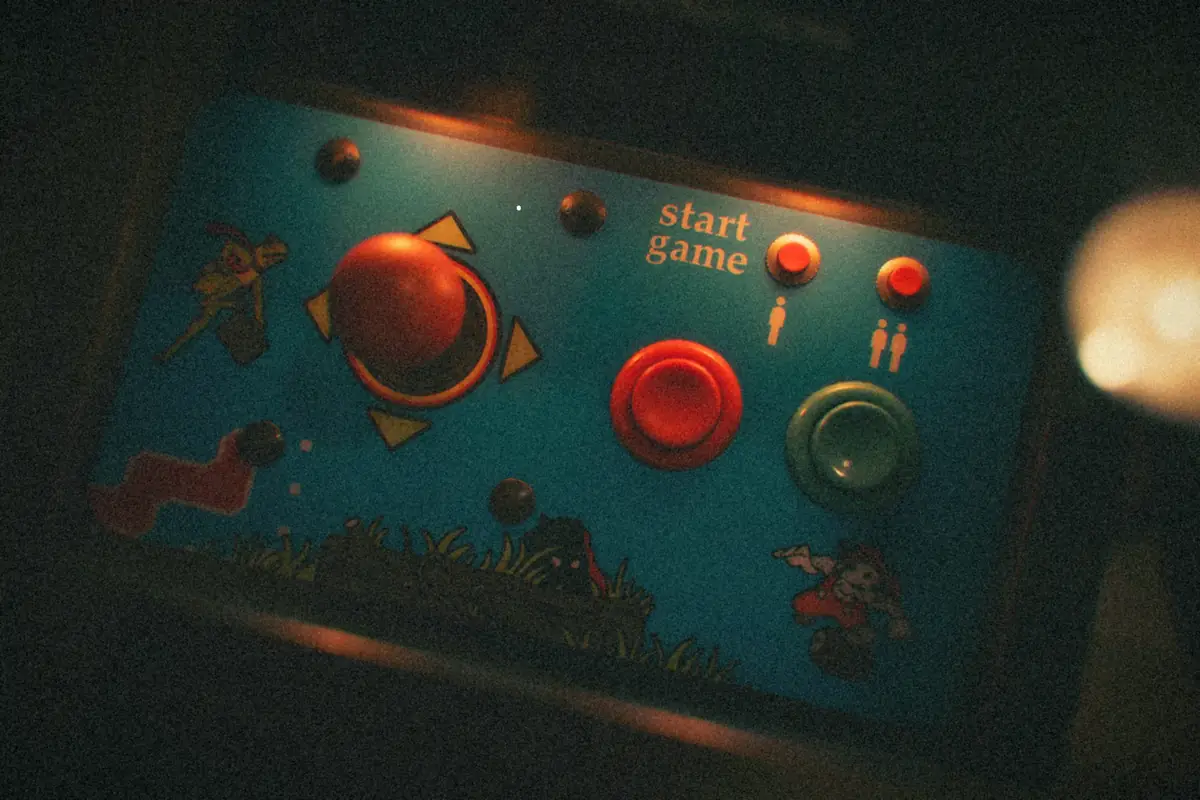 The worn control panel of a classic early-'80s arcade cabinet, with a red ball-top joystick, two big buttons and painted cartoon artwork.