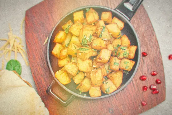 Crispy golden potato cubes tossed with herbs in a small cast iron skillet on a wooden board.