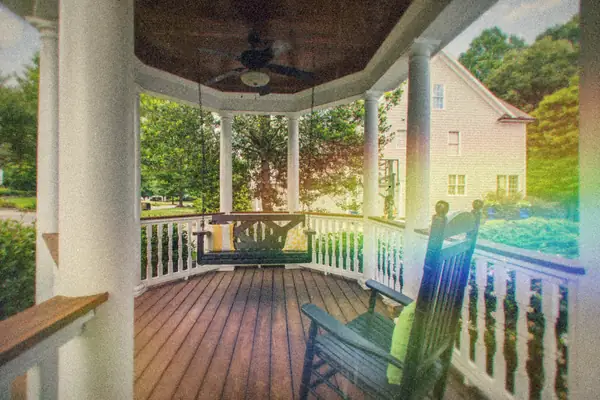 A wide wooden front porch with a hanging swing and rocking chair among green trees.