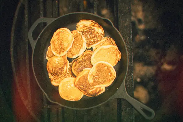 Small pancakes cooking in a cast-iron skillet, seen from above.