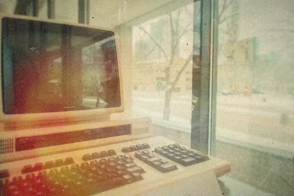 A vintage computer and keyboard sitting by a window with snow outside.